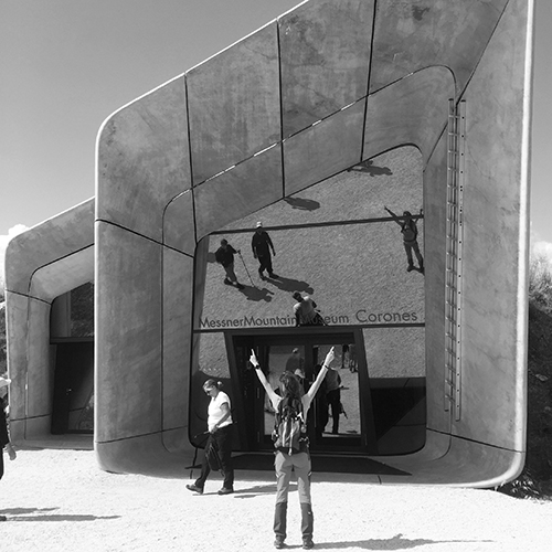 The concrete building of a mountain museum, with a person standing in front of it with raised arms