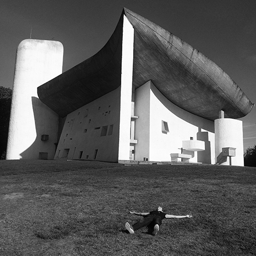 A chapel with a curved roof and a white tower, with a person lying on the grass in front of it