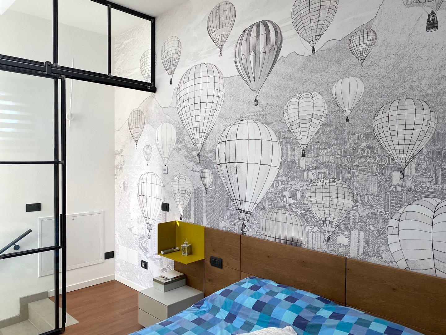 A bedroom with a large hot-air balloon wallpaper, a wooden headboard and a glass and iron partition