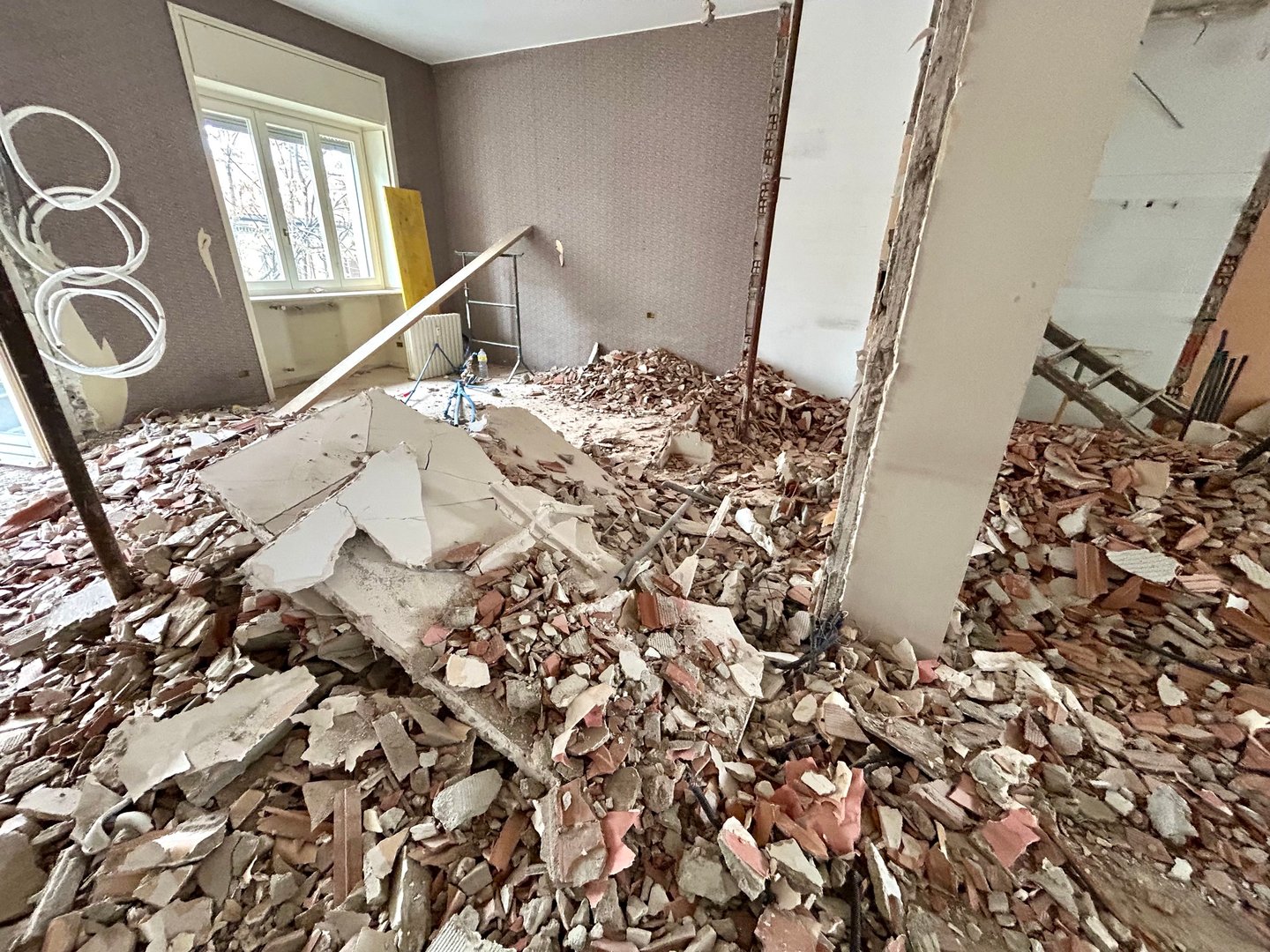 An apartment during demolition: rubble on the floor, walls stripped of their partitions and a window in the background